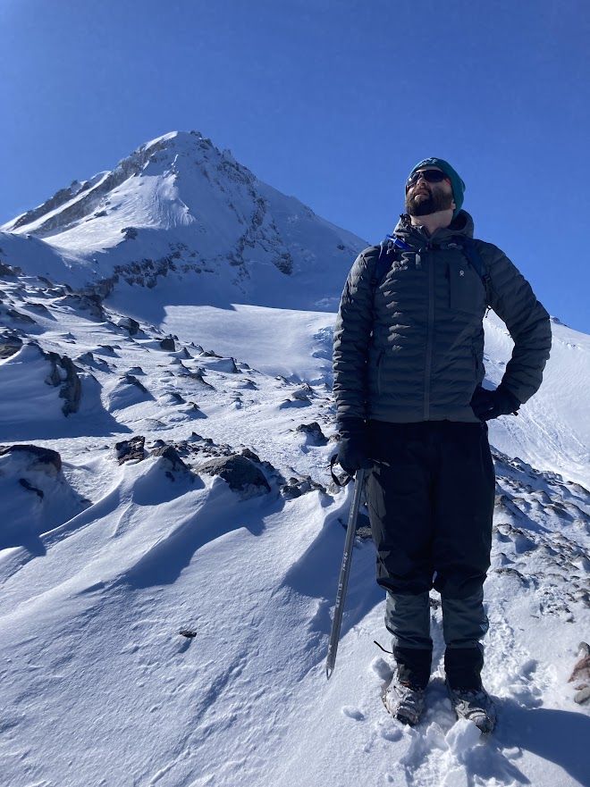 The site's author in a winter coat holding an ice axe with a snow-covered mountain peak in the background